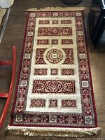 Full view of the small runner rug showing the overall burgundy and cream patterned design and fringed ends.
