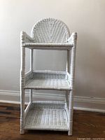 Front angled view of small white wicker shelf showing three shelves and arched backrest