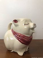 Side view of ceramic pig jug showing maroon scarf, ears, and brown hooves.