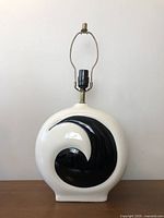 Front view of a vintage ceramic table lamp with white body and black swirl design in glossy finish, brass fitting and black socket visible at top.