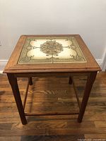 Front view of the wooden side table showing square top with decorative ceramic tiles and teak frame.