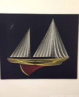 Full view of vintage string art showing a sailboat with white sails, yellow boat outline, and red hull on dark fabric background.