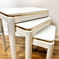 Stacked view of three vintage white lacquer nesting tables with brass edge detailing, showing their nested arrangement and rounded corners.