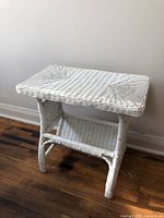 Front angled view of white wicker side table showing woven wicker tabletop and curved legs.