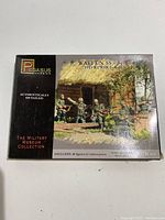 Front of the box showing the product title, brand and detailed image of figures with a rural wooden house scene