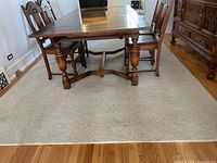 Photo showing the full carpet under a wooden dining table, highlighting the beige color and texture of the carpet as well as its approximate size.