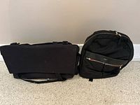 Photo of two black bags side by side on carpet, one duffle bag and one backpack