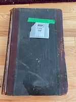 Front cover of the worn scrapbook with leather spine and black textured cover showing a label taped to the front.