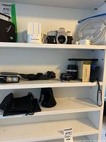 Shelf with Minolta camera, Nikon flash units, lenses, dust bags, and charging accessories.