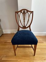 Front view of vintage wooden chair with detailed carved backrest and blue upholstered seat.