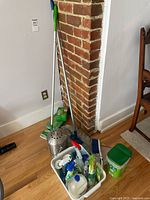 Photo showing two mops leaning against a brick wall corner with cleaning wipes on floor and metal dome-shaped object nearby.