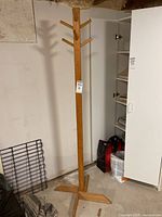 Full view of wooden coat rack showing eight pegs over four sides and four-legged base, positioned in basement against wall.