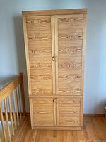 Front view of the closed wooden cupboard showing natural wood grain double doors on upper and lower sections.