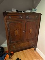 Front view of the antique McLagan gentleman's dresser showing the two small upper drawers, two paneled doors with decorative inlay, lower drawer, and metal drawer pulls.