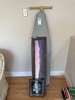 Ironing board standing against wall with two framed art pieces positioned leaning on it