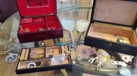 Wide shot showing two jewelry boxes containing assorted costume jewelry including brooches, rings, earrings.