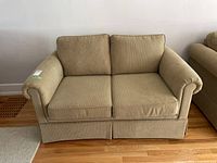 Front view of beige love seat couch showing rolled arms, skirted base, and two seat cushions with slight unevenness.
