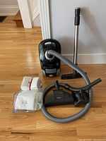 Overview of vacuum, hose, wand, floorhead, upholstery nozzle, and filter bags arranged on hardwood floor