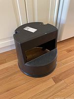 Front angled view of the black plastic step stool showing the textured step surface and cutout hand grips.