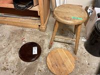 Wooden stool and two wooden round bases shown on concrete floor near shelving unit