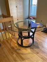 Round glass top table with bamboo style dark wood frame base. Decorative fabric table cloth is folded on the table.