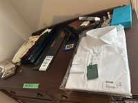 Photo showing white dress shirt, various belts, cuff links boxes, and other tuxedo accessories arranged on wooden surface.
