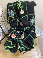 Full view of black crocheted afghan draped, showing floral motifs and green grid
