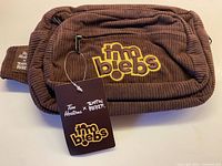 Front view of brown corduroy fanny pack showing embroidered tim biebs logo and hang tag