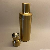 Cocktail shaker standing beside double-ended jigger