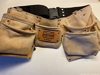 Front view of suede tool belt showing dual large pouches, brand patch, and nylon belt