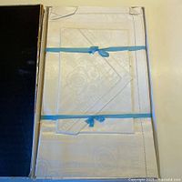 Boxed linen set showing folded tablecloth and napkins tied with blue ribbon