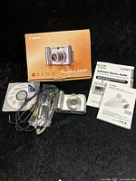 Canon PowerShot A630 digital camera with box, software CD, cables, and manuals laid out on black surface.