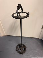 Full view of the entire cast iron ashtray stand against white wall and grey floor.