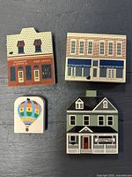 Four Cats Meow Village collectible wooden buildings and a hot air balloon monument arranged on a gray background showing front details and sizes.