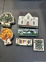 Full view of the Cats Meow Village wooden collectibles including buildings, trees, clothesline, and plant pieces on a dark surface.