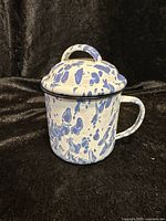 Side view of white enamelware mug with blue splatter pattern and handle, showing lid on top