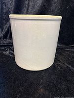 Full side view of the farmhouse stone crock against black fabric background showing smooth light beige surface and unglazed rim.