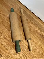 Two vintage wooden rolling pins laid side by side on wood floor, showing size and condition.