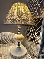 Full view of the lamp powered on, showing milk glass base with painted yellow rose and lace doily covered lampshade.