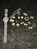 Full lot view with multiple pairs of earrings and the Marvin the Martian watch spread on black fabric background.