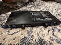 Front-side diagonal view showing top labeling and overall condition of the rectangular black metal unit on carpet.