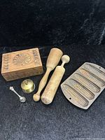 Full view of lot contents including wooden box, two wooden rolling pins, brass stamp roll holder, souvenir spoon, and cast iron cornbread mold.