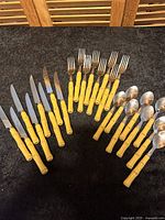 Full set of 24-piece vintage flatware with yellow faux bamboo textured handles and stainless steel heads, including knives, forks, and spoons.