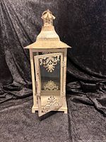 Full front view of metal candle lantern showing door with ornamental scrollwork and textured finish.
