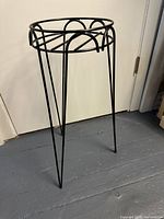 Photo showing full side view of the black metal plant stand with three legs and circular top.