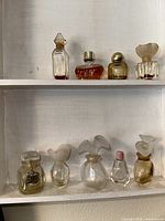 Front view of 10 miniature collectible perfume bottles arranged on two shelves, showing various sizes, shapes, and cap designs