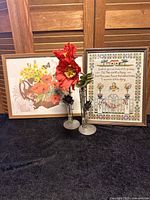 Photo shows two framed art pieces and two metal sunflower vases each with resin poppies on a black surface against wooden paneling.