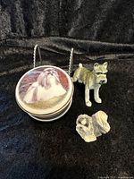 Wide shot showing all three items: Schnauzer figurine, covered trinket dish with Shih Tzu image, and small Shih Tzu figurine, on black fabric background.