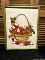 Full view of framed crewelwork featuring strawberries and flowers in basket with green faux bamboo frame.