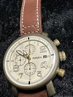 Close-up of the watch face showing the cream dial, gold-plated case, three sub-dials, date window, and Fossil branding.